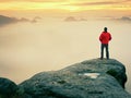 Man hiker at mountain peak. Marvelous daybreak in autumn misty landscape. Sun hidden in clouds