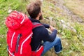 Man hiker with red backpack sitting on ground