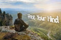 Man hiker sitting on top of mountain meeting sunrise. Free Your Mind inscription sign in form of clouds.