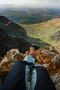 Man hiker sitting on the top of mountain rocks. Beautiful weather with Scotland nature. Detail of hiking boots on the difficult pa Royalty Free Stock Photo