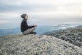 Man hiker sitting in a yoga pose at the peak of the mountain in the summer. Meditation after a long climb on a mountain