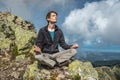 Man hiker sitting in a yoga pose at the peak of the mountain in the summer. Meditation after a long climb on a mountain