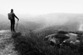 Man hiker with trekking poles and red backpack on rock. Old heather bushes grows in rock