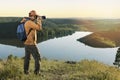 Man hiker in a vibrant yellow coat with a backpack and camera taking photo of sunset mountains. Royalty Free Stock Photo