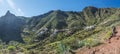 Man hiker watching at scenic landscape with Imada village at hiking trail Barranco de Guarimiar Gorge. Green mountain