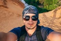 Man Hiking makes a selfie on the camera face in sunglasses and a bandana
