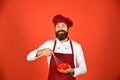 Man or hipster with beard holds kitchenware on red background.