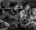 Man with hipster beard playing guitar at college party. Musician rehearsing new song. Bearded man entertaining two blond Royalty Free Stock Photo