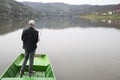 Man With His Back Towards Camera Fishing From The Boat Reeling String And Waiting Fish To Take A Bait Water Reflection