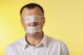 A man with his eyes and mouth sealed with a painting tape on a yellow background, the concept is not afraid to tell the truth