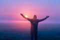 A man with his hands in the air stands in the field at sunrise Royalty Free Stock Photo