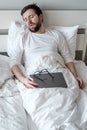 Man with a laptop fell asleep sitting in bed, he worked remotely all night and was tired. Concept of quarantine. Royalty Free Stock Photo