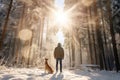 A man and his pet dog walking though a snowy forest on sunny winter day. Adventurous young man and his dog on a walk. Hiking and