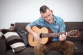 Man in his 50s sitting on couch and playing guitar Royalty Free Stock Photo