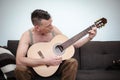 Man in his 50s sitting on couch and playing guitar Royalty Free Stock Photo