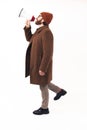 Man in his 30s using megaphone to yell - dressed in a camel coat and stylish boots - profile shot on white background - Royalty Free Stock Photo