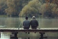 Man and his senior father fishing on a pier while relaxing in freshwater. Copy space available. Royalty Free Stock Photo