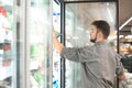 Man in his shirt takes his hand frozen foods from the refrigerator in the supermarket. The buyer selects the products in the Royalty Free Stock Photo