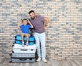 Man and his son with suitcases near brick wall