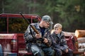 Man at his truck with his son in the forest. Hunter teaches young boy how to use shotgun rifle.
