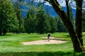 Man hitting a golf ball out of a sand trap on a wooded golf course