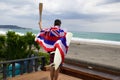 Man hold a torch used in large sporting event , with Hawaiian flag and surfboard.