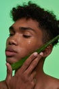 Man holding aloe vera leaf on his face with lotion