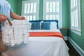 A man holding a basket of organized clean rolled white towels for guests near a bed in a guest bedroom Royalty Free Stock Photo