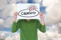 Man holding billboard with creativity text while standing against sky