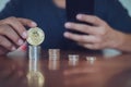 Man holding bitcoin while using smartphone with selective focus on bitcoin.