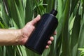 Man holding black bottle of shampoo against green leaves, sun lights