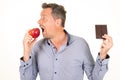 Man holding black dark chocolate bar prefers eating juicy red apple in white background