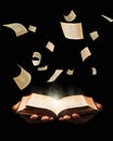 Man is holding book with flying pages and radiance light on black background. learing, reading, knowledge concept. Royalty Free Stock Photo