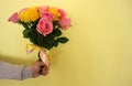 A man holding a bouquet of yellow and pink roses on a light-yellow background. Royalty Free Stock Photo