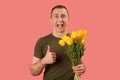 Man holding bouquet of yellow tulip flowers shows thumbs up and screaming with open mouth. Isolated on pink background Royalty Free Stock Photo