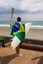 Man holding Brazilian flag and surf board with a torch used in large sporting event.