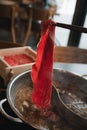 Man holding chopsticks with a piece of boiled sliced raw beef