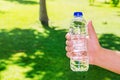 Man holding clear drinking water in a plastic bottle on a green grass summer background Royalty Free Stock Photo