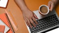 Man holding coffee cup and using laptop computer on brown leather. Royalty Free Stock Photo