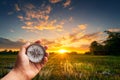 A man holding compass on hand at field and sunset for navigation guide