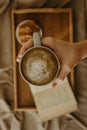 Man holding a cup of coffee on a blurred book and croissant on a wooden tray