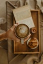 Man holding a cup of coffee on a blurred book and croissant on a wooden tray