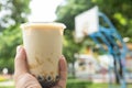 man holding cup of iced milktea with tapiocas and guiling jelly in front of outdoor basketball court horizontal composition