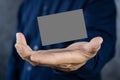 Man holding a dark gray business card against a concrete wall Mature male hand holding a blank business card in front of the Royalty Free Stock Photo