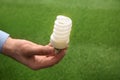 Man holding energy saving bulb for lamp against green grass Royalty Free Stock Photo