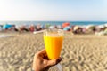 A man holding a fresh glass of orange juice with a straw in front of the beach Royalty Free Stock Photo