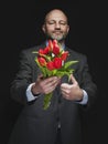 Man holding fresh red tulip bouquet in his hands. Model is bald with grey beard, wearing classic grey suit. Handsome male with