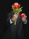 Man holding fresh red tulip bouquet and red heart in his hands. Model is bald with grey beard, wearing classic grey suit. Handsome