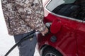 Man holding fuel pump nozzle with filling benzine oil in red car at self-service petrol station