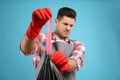 Man holding full garbage bag against light blue background, focus on hand Royalty Free Stock Photo